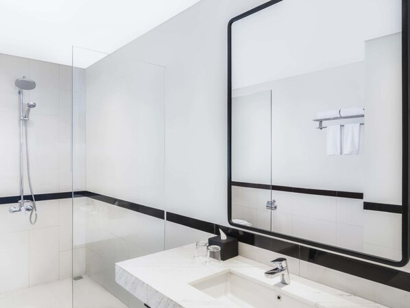 Une salle de bain moderne avec une douche à l’italienne en verre, un lavabo blanc doté d’un plan de travail noir et un grand miroir avec un cadre noir.