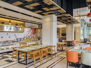 Un restaurante moderno con una larga mesa común, mesas individuales y una zona de cocina con salpicadero de azulejos.