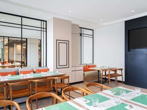 Un espace repas moderne avec des tables et des chaises en bois, un grand miroir et un mur d’accent de couleur foncée.