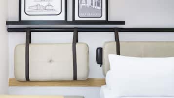 Quarto de hotel com uma cama, uma mesa de cabeceira e duas quadros na parede.