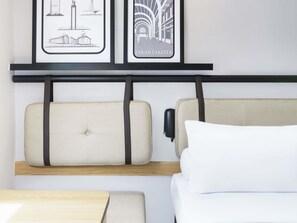 Ett hotellrum med en säng, ett sängbord och två inramade tavlor på väggen.