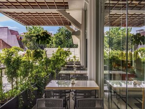 Un espace de restauration en plein air avec des tables et des chaises en verre, entouré de verdure et offrant une vue sur le paysage urbain.