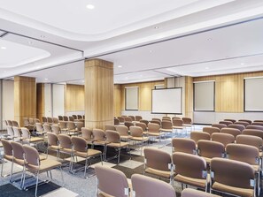 Une salle de conférence avec des rangées de chaises, un grand écran et un lambris en bois.