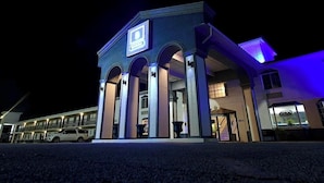 A hotel with a prominent entrance, a visible staircase, and a parking area with a white car. - Boardwalk Suites Lafayette (Lafayette)