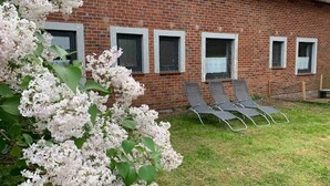 Un bâtiment en briques avec quatre fenêtres, une pelouse verdoyante et trois chaises longues.
