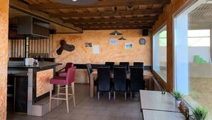 Un intérieur rustique avec un plafond en bois, un coin bar avec des tabourets, une table à manger avec des chaises et une grande fenêtre.