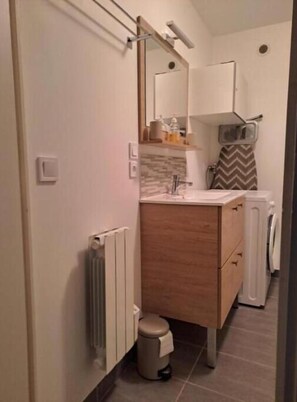 A compact bathroom with a wooden vanity, a mirror, a towel hanging on the wall, and a radiator. - Joli T1 Hyper Centre Rochefort (Rochefort)