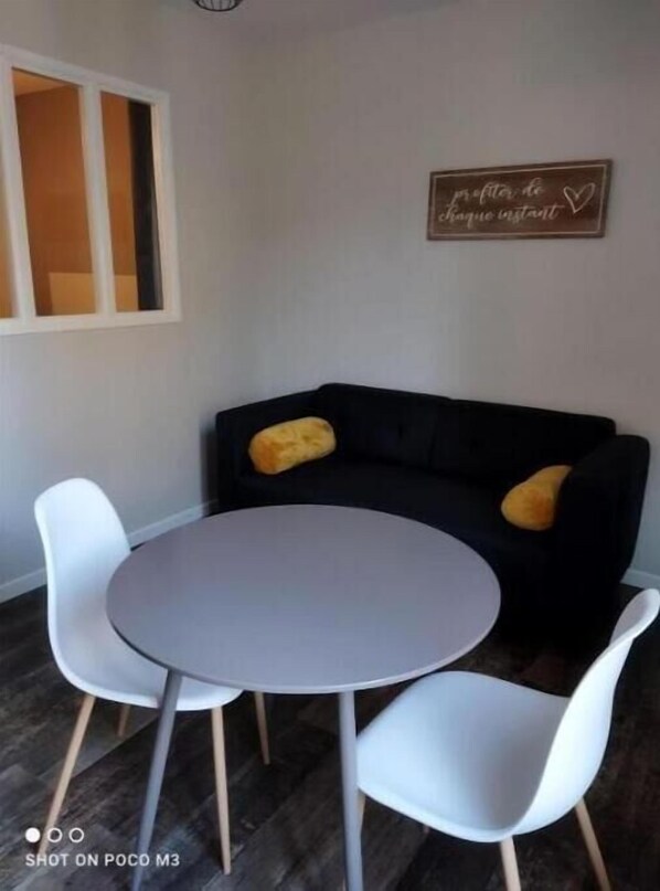 A modern room with a round table and two white chairs, a black sofa with yellow cushions, and a wall sign. - Joli T1 Hyper Centre Rochefort (Rochefort)