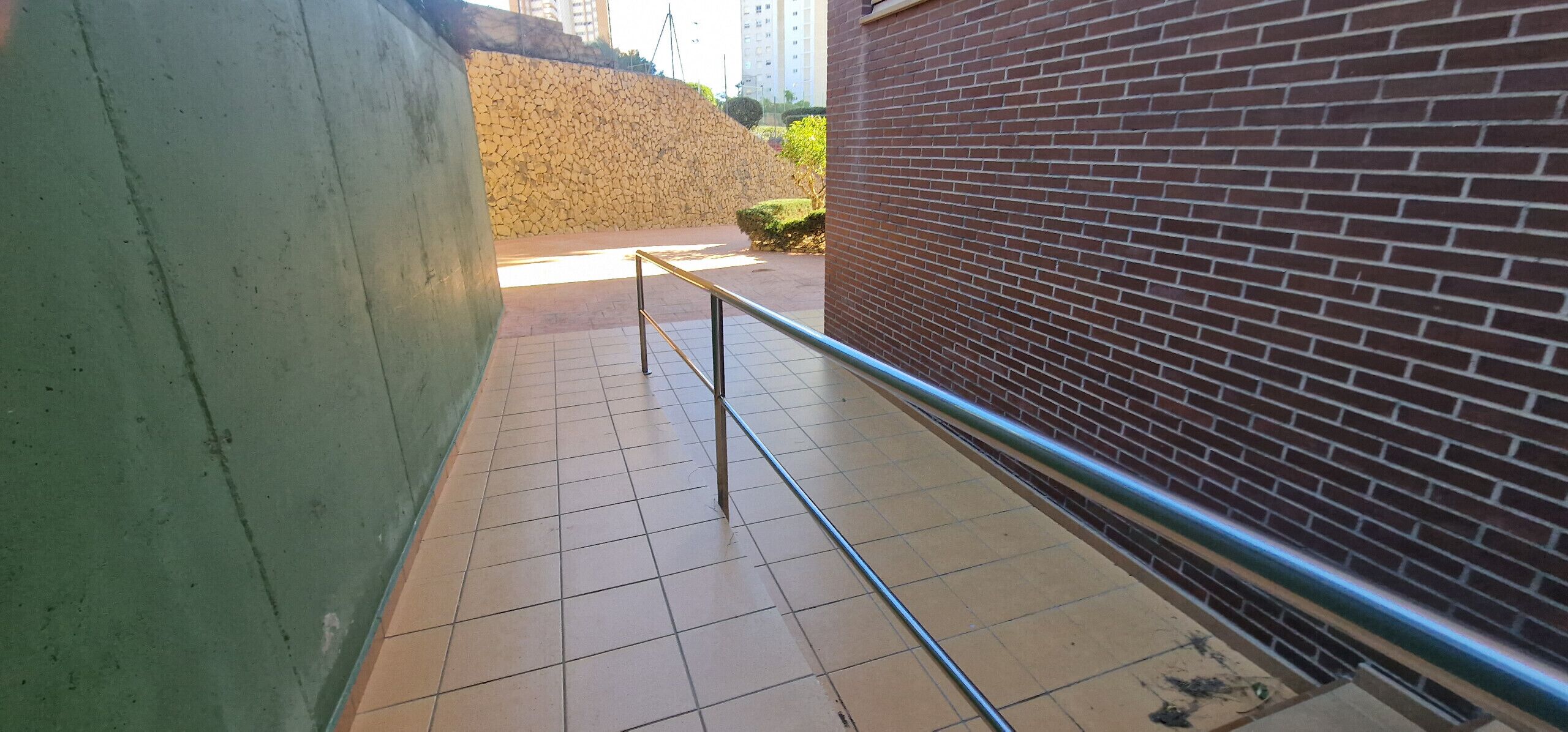 A corridor with tiled flooring, a metal railing, and a brick wall.