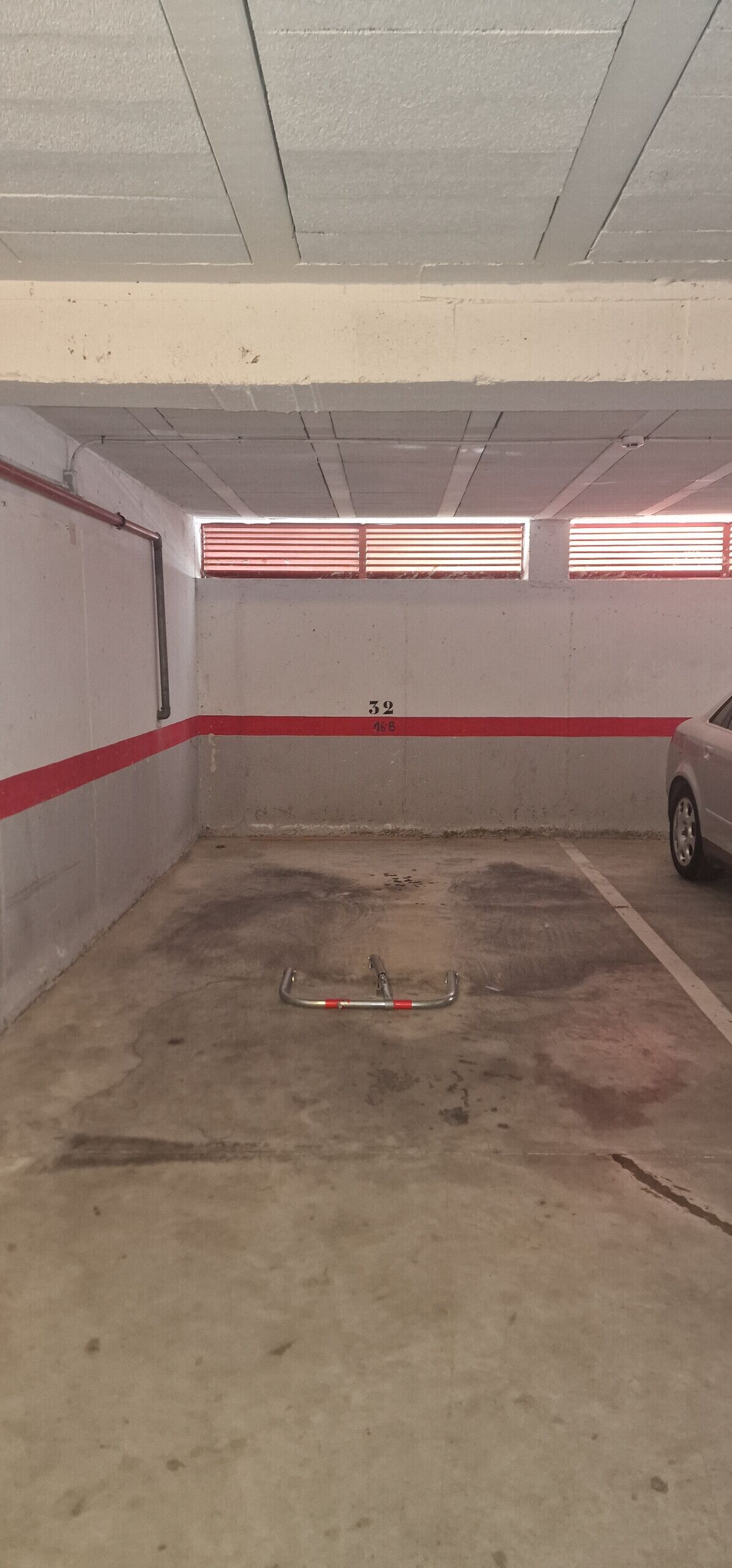 Een parkeergarage met betonnen vloeren, rode en witte wanden en een metalen barrière in het midden.