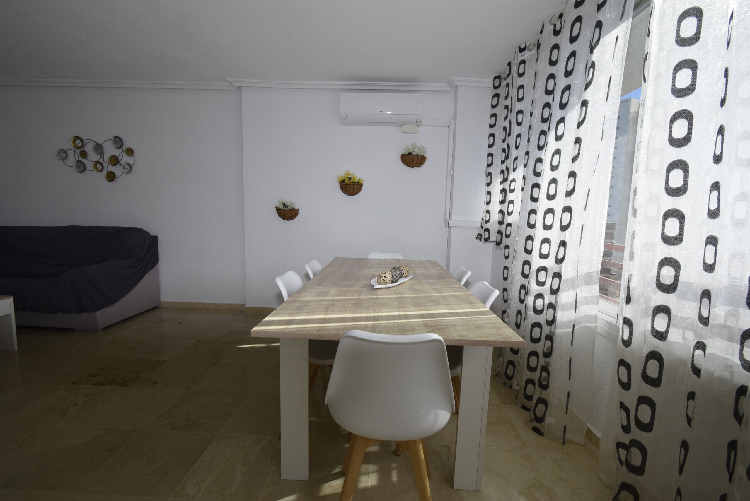 A dining area with a wooden table, white chairs, and a ceiling air conditioner.