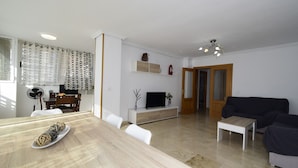 A modern living room with a sofa, a TV, and a dining area with a table and chairs.