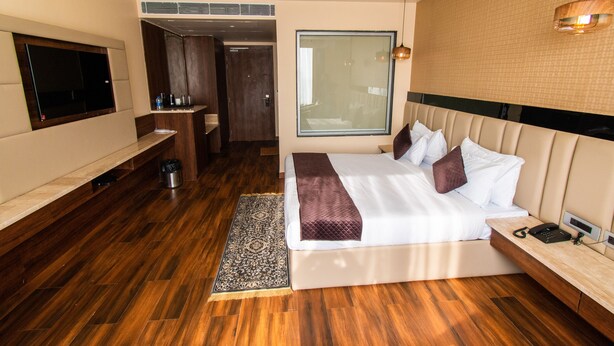 Habitación de hotel moderna con una cama grande, televisión, minibar y baño visible a través de una puerta abierta.