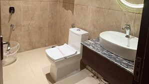 Un baño moderno con inodoro, bidé, lavamanos y espejo con luz circular.