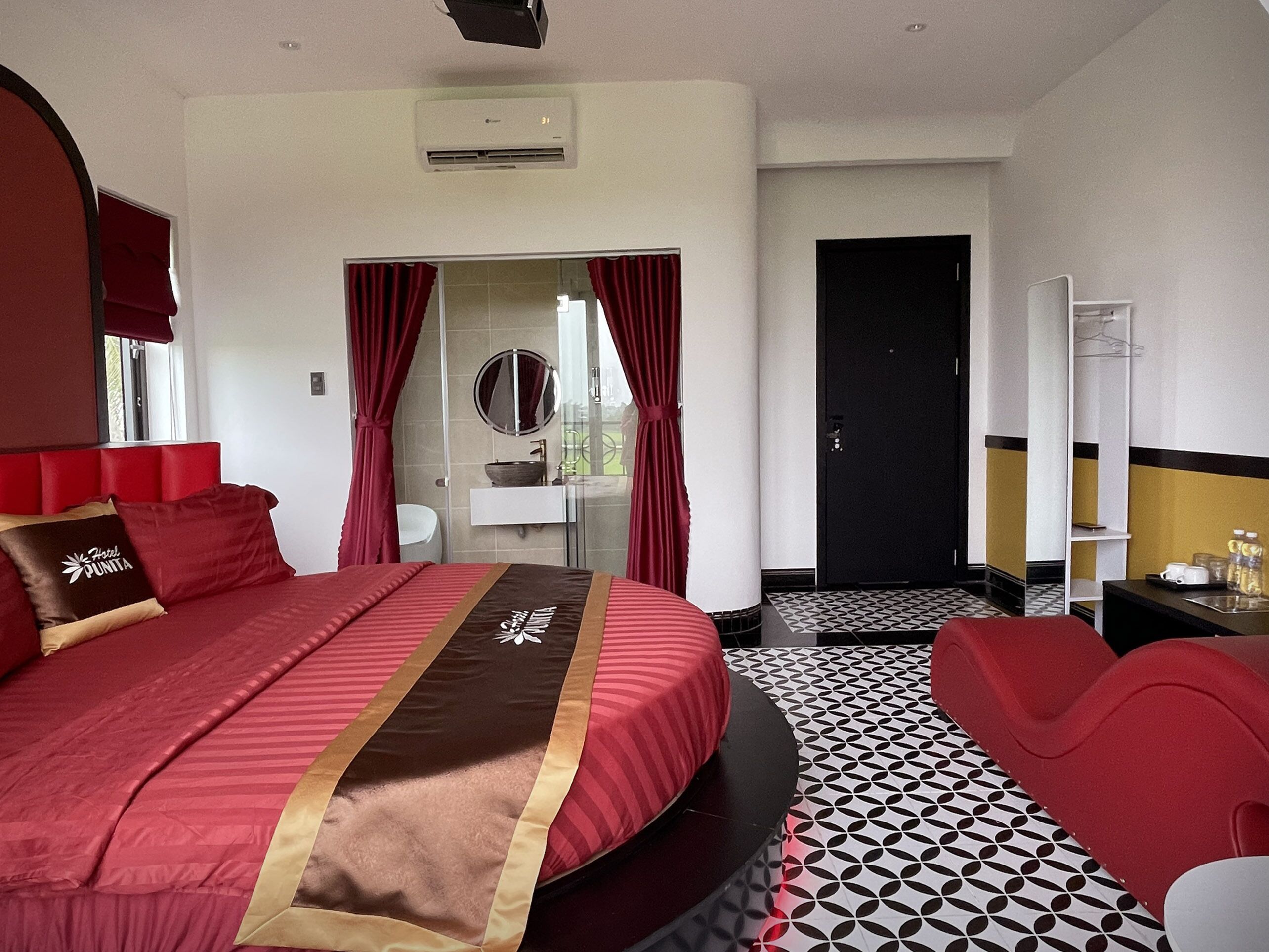 Hotelkamer met een groot bed, een ronde spiegel, een badkamer met een wastafel en een deur naar een andere kamer.