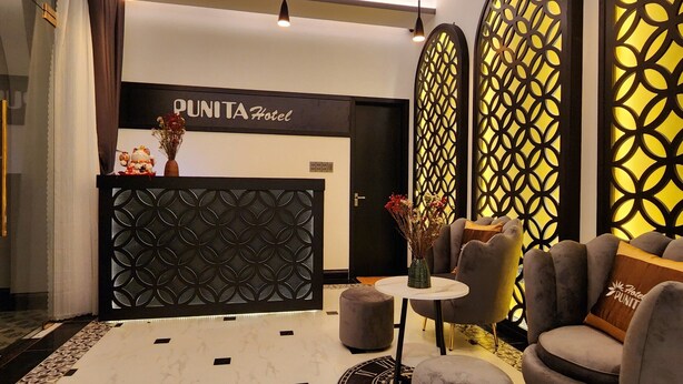 A reception area with a modern design, featuring a reception desk, seating area with armchairs, and decorative elements like a vase with flowers and a patterned wall. - Punita Hotel (Da Nang)