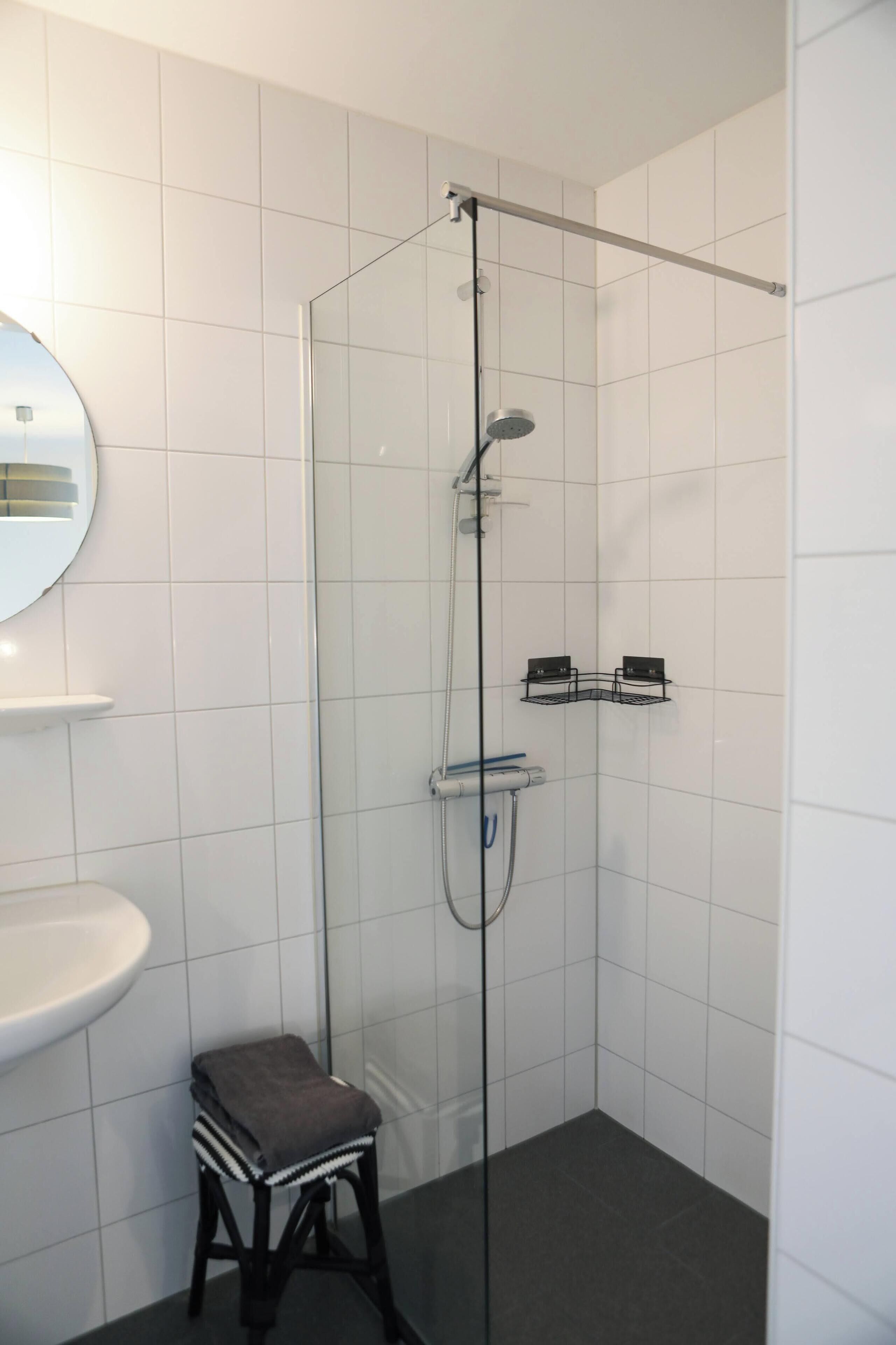 A modern bathroom with a glass-enclosed shower, a white sink, and a small stool.