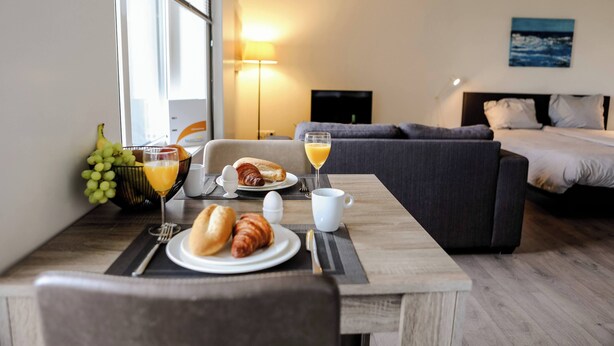 A hotel room with a dining table set for breakfast, a sofa, and a bed. - Appartement 18 wemeldinge (Wemeldinge)