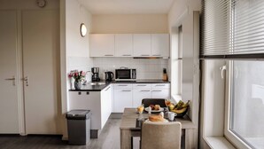 A compact kitchen with white cabinets, a microwave, a coffee maker, and a dining area with a table and chairs. - Appartement 18 wemeldinge (Wemeldinge)