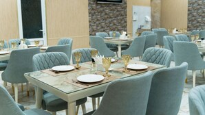 Un comedor con varias mesas dispuestas para comensales, con sillas tapizadas en azul claro y copas con detalles dorados.