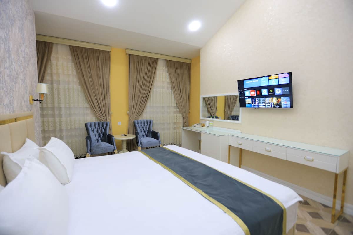 A hotel room with a large bed, two armchairs, a small table, a desk, and a TV mounted on the wall.