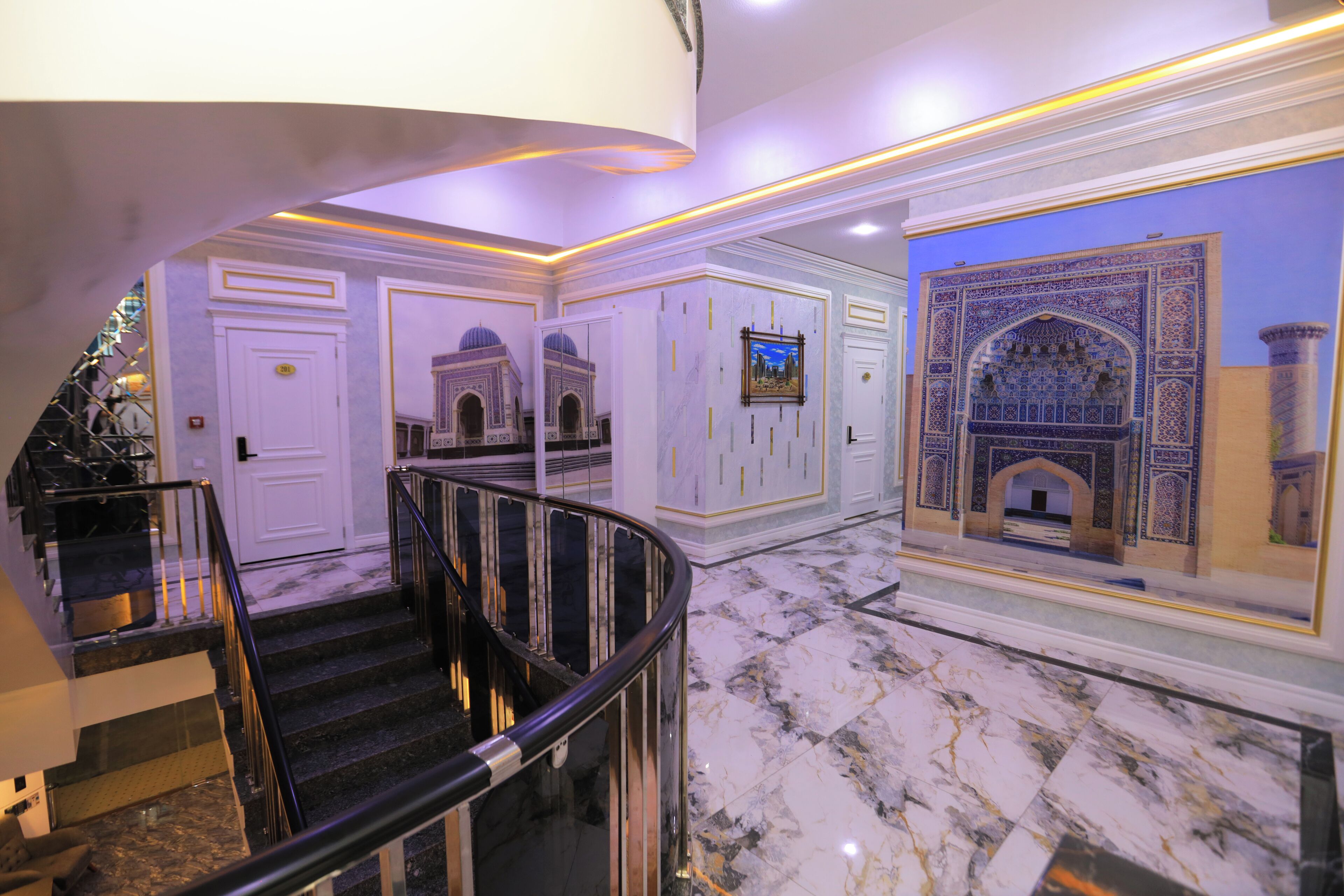 A grand hallway with marble floors, a curved staircase, and ornate wall decorations.