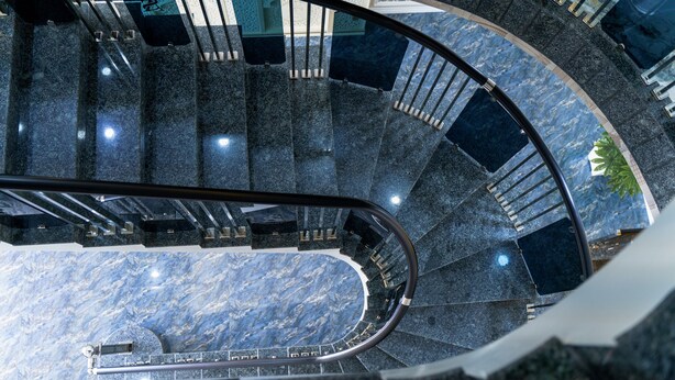 Una escalera curva con barandilla, escalones de mármol y balaustrada de vidrio.