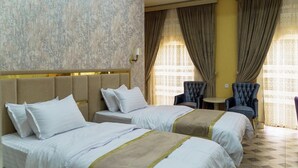 Habitación de hotel con dos camas, una mesita, dos sillas y un detalle decorativo en la pared.