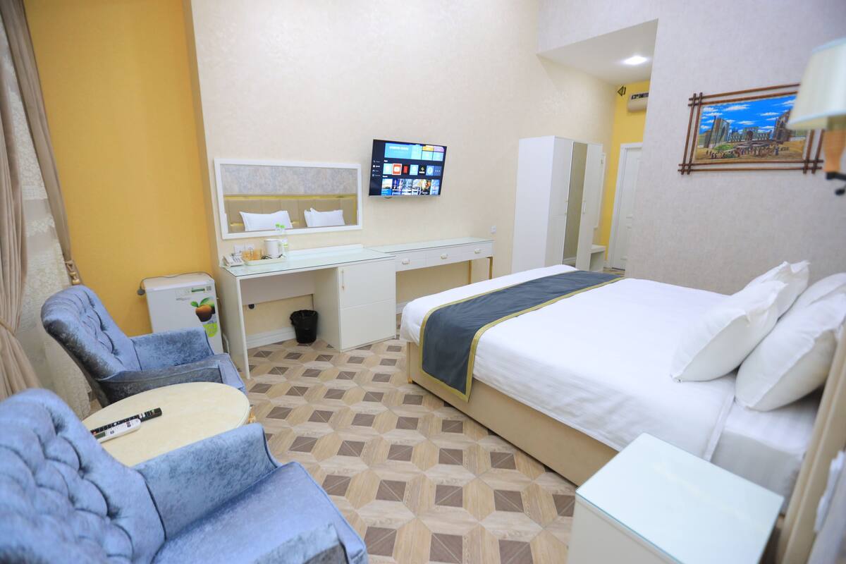 A hotel room with a bed, a desk, a chair, a TV, and a painting on the wall.