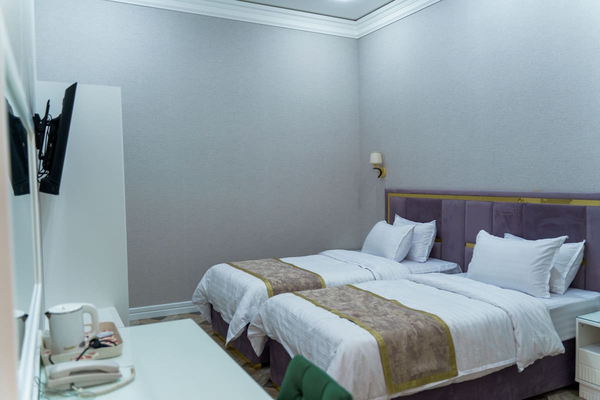 A hotel room with two beds, a small desk, a mirror, and a wall-mounted lamp.