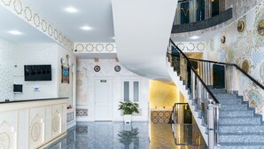 Un vestíbulo con suelo de mármol, mostrador de recepción, escalera y diseños decorativos en las paredes.