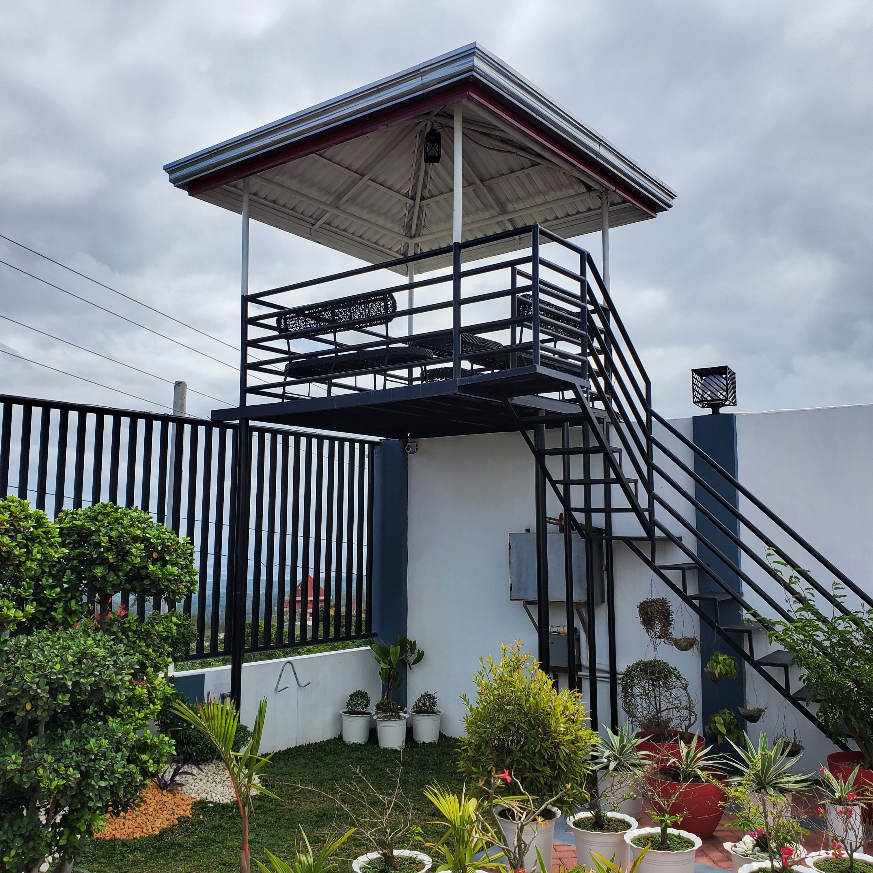Estrutura externa de vários níveis com escada de metal, cercada por plantas em vasos e uma parede branca.