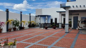 A courtyard with a red brick floor, potted plants, and a white building with a blue door. - MyFantasyResort.com Room A - Occupancy 2-3 Guests (Lemery Ph)
