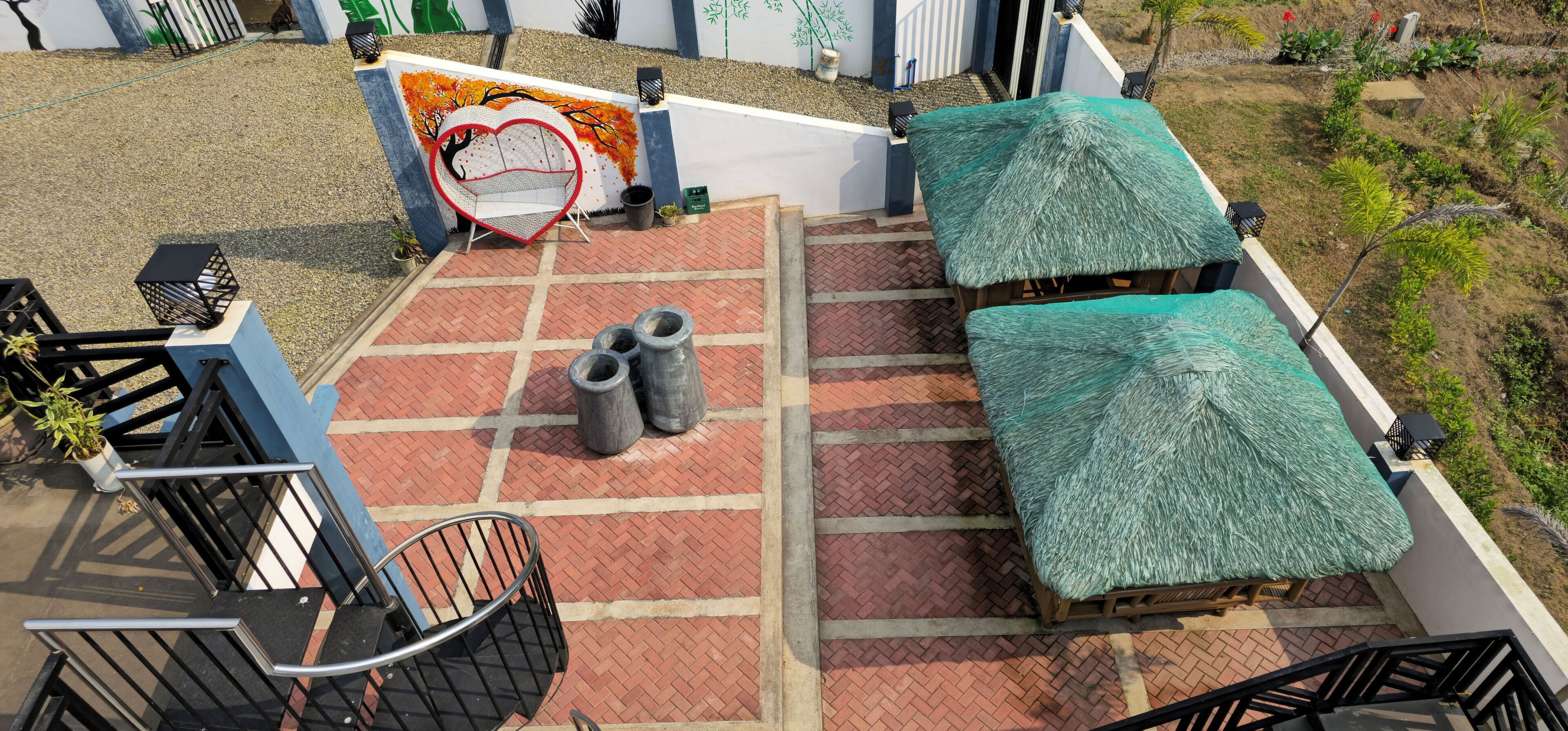 A rooftop terrace with a red heart-shaped seating area, two thatched umbrellas, and a staircase leading to the upper level.