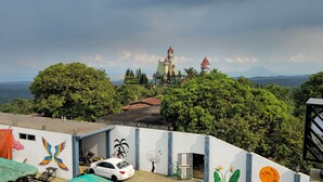 A view of a castle-like structure with a red roof, surrounded by lush greenery and mountains in the background. - MyFantasyResort.com Room A - Occupancy 2-3 Guests (Lemery Ph)