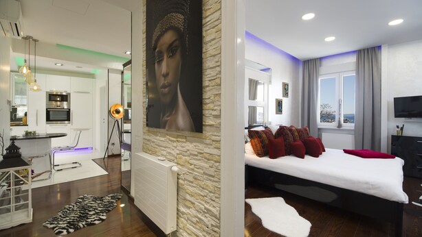 A modern bedroom with a large bed, a view of the city, and a separate living area with a TV and seating. - Central Station Art Apartment (Split)