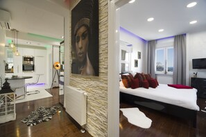 Un dormitorio moderno con una cama grande, vistas a la ciudad y una sala de estar independiente con televisión y asientos.