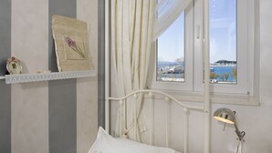 A bedroom with a bed, a window with a view of a body of water and buildings, a bedside lamp, and a decorative item on the wall. - Central Station Art Apartment (Split)