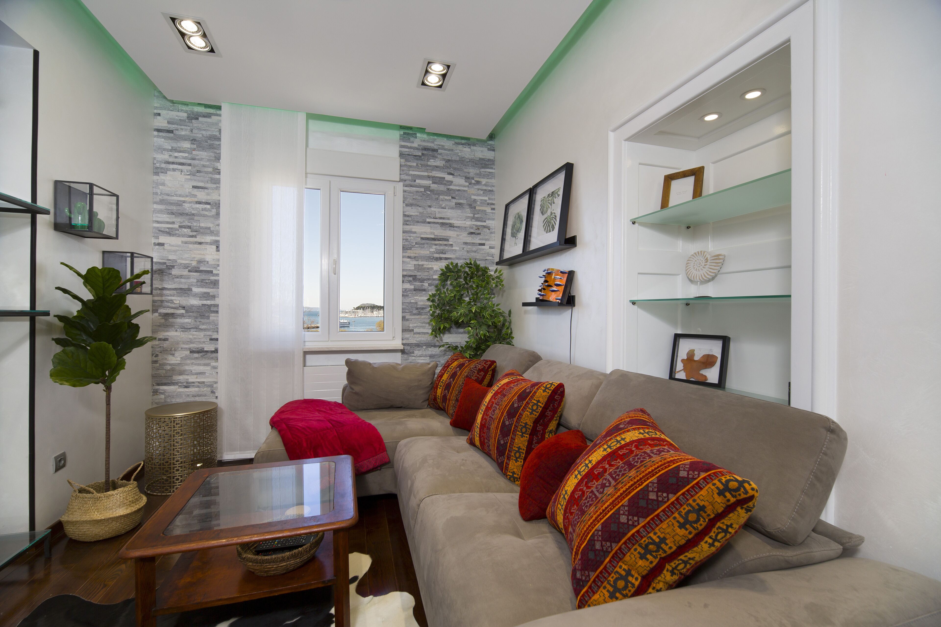 Un salón con un sofá color beige, cojines estampados, una mesa de centro de cristal y vistas de la ciudad a través de una ventana.