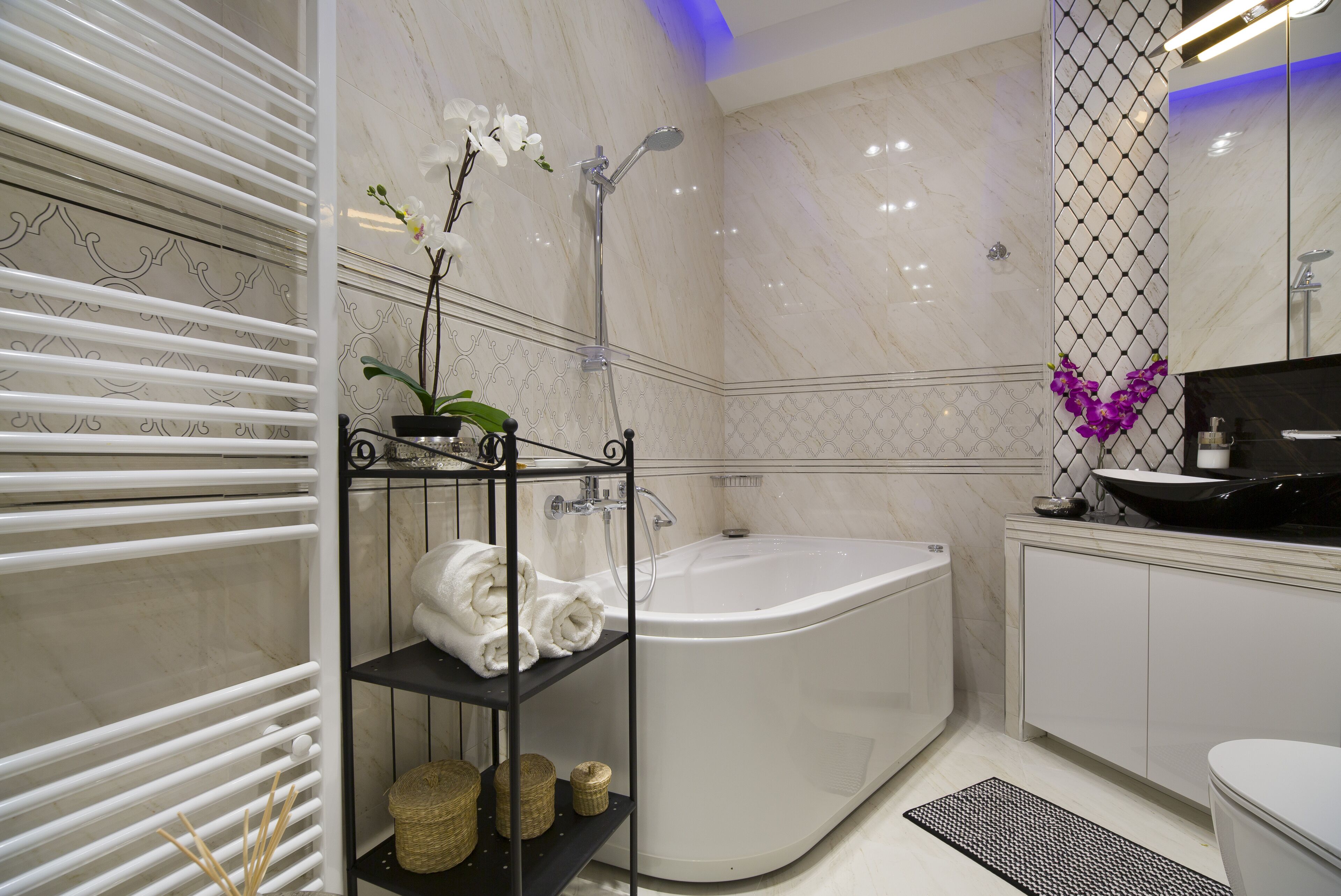 A modern bathroom with a freestanding bathtub, a black metal shelf with towels, and a decorative orchid plant.