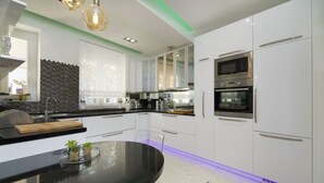 A modern kitchen with white cabinets, a black countertop, and a central island with chairs. - Central Station Art Apartment (Split)