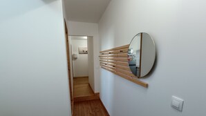 A hallway with wooden flooring, a round mirror on the wall, and a wooden slat shelf. - La Terrasse des Augustins (Limoux)