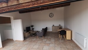 A compact living space with a tiled floor, a sofa, a dining table, a TV, and a radiator. - La Terrasse des Augustins (Limoux)