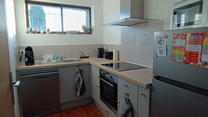 A compact kitchen with a dishwasher, oven, and refrigerator. There's a window above the sink and a microwave on the countertop. - La Terrasse des Augustins (Limoux)
