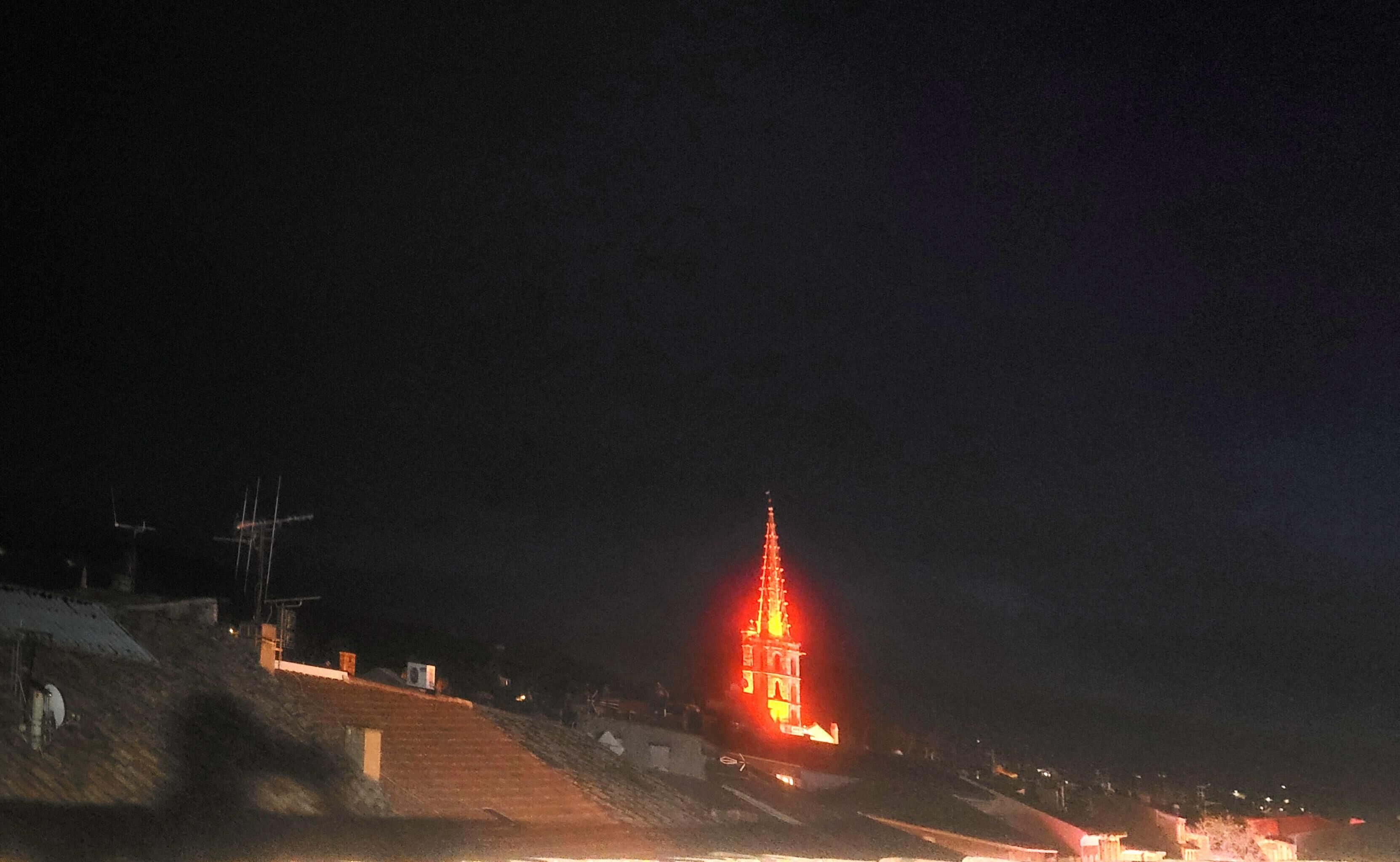 Vue nocturne d’un immeuble dont la tour, particulièrement imposante, est illuminée en rouge.