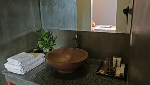 Un baño con un lavamanos grande de estilo rústico, toallas dobladas con cuidado, una planta en maceta y artículos de aseo en una bandeja.