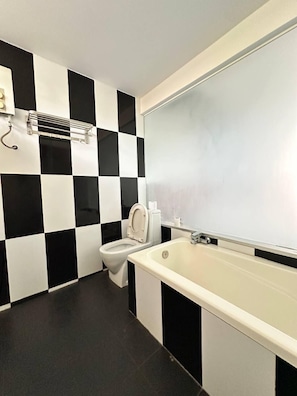 Un baño con pared de azulejos blancos y negros en damero, un inodoro, un lavabo y un perchero para toallas.