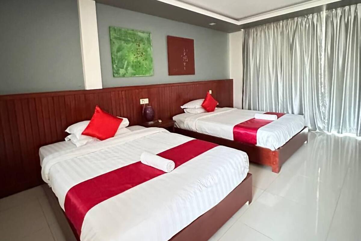 A hotel room with two beds, a wooden headboard, a green abstract painting, and a red pillow.