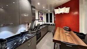 A modern kitchen with stainless steel appliances, a marble countertop, and a red accent wall. - Luxury apartment next to the Trocadéro (Paris)