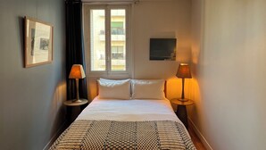 A bedroom with a bed, two bedside lamps, a window, and a picture on the wall. - Luxury apartment next to the Trocadéro (Paris)